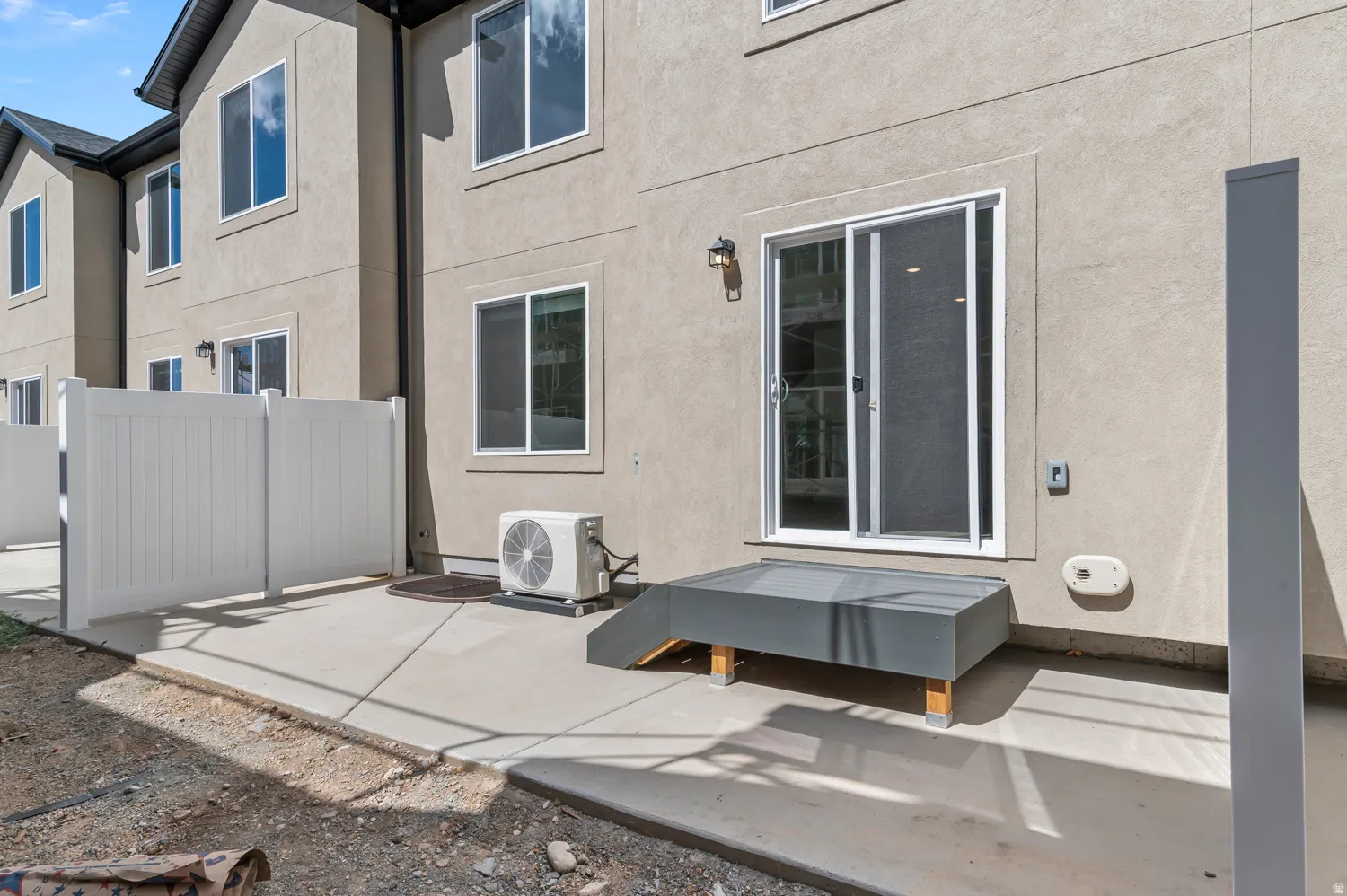 Concrete patio featuring a privacy fence, sliding glass door, and exterior wall sconce