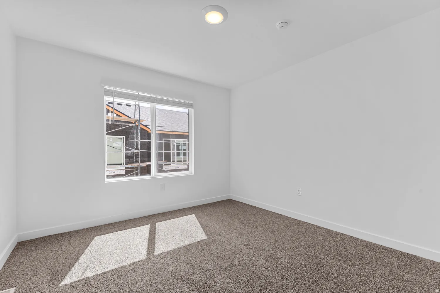 Spacious room featuring clean white walls, neutral carpeting, a large window with blinds, and recessed lighting