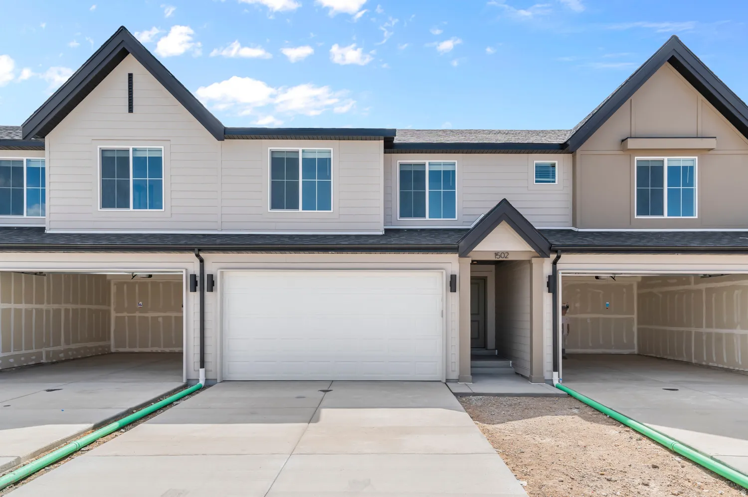 Modern multi-unit residence featuring a gabled roofline, light-toned siding, attached garages, and a paved driveway