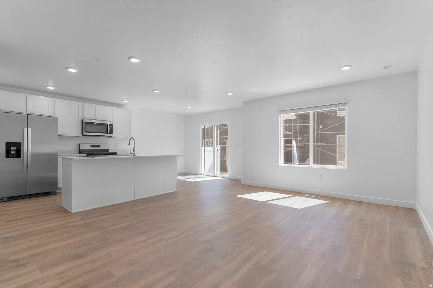 Open-concept living space featuring wood-finish flooring, recessed lighting, and a kitchen with stainless steel appliances