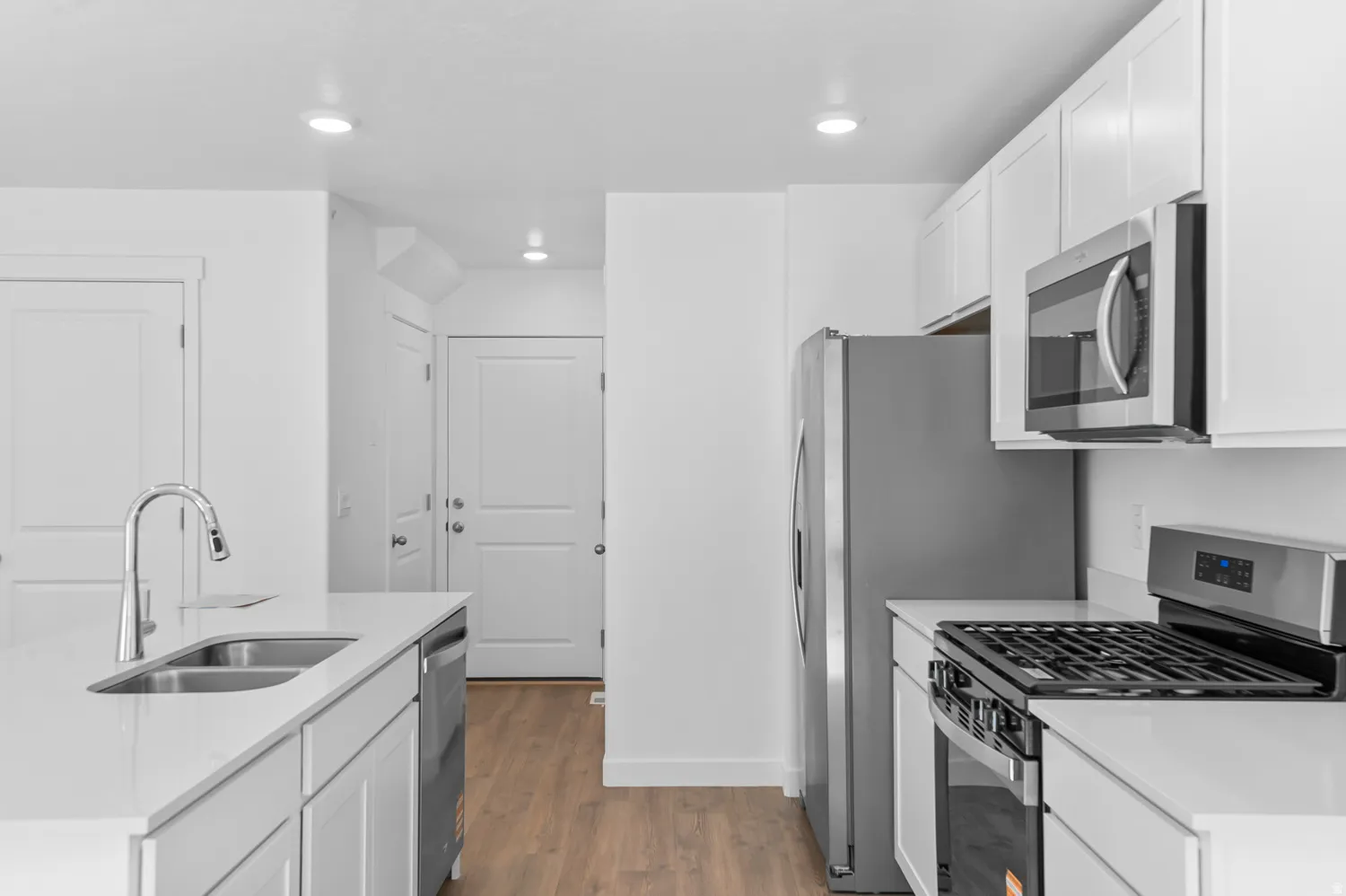 Modern kitchen featuring white cabinetry, stainless steel appliances including a gas range and built-in microwave, a double basin sink with a gooseneck faucet, light-toned countertops, and recessed lighting