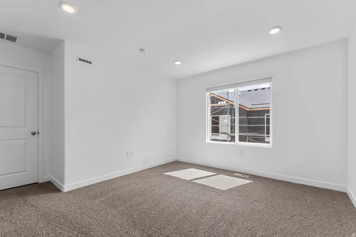 Carpeted room featuring a white interior door, recessed ceiling lighting, a rectangular window with white trim, and white baseboards