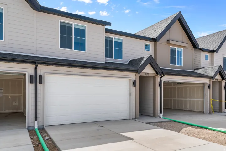 Contemporary townhome community featuring a two-car attached garage with white paneled doors, concrete driveway, and neutral exterior finishes in cream and taupe tones