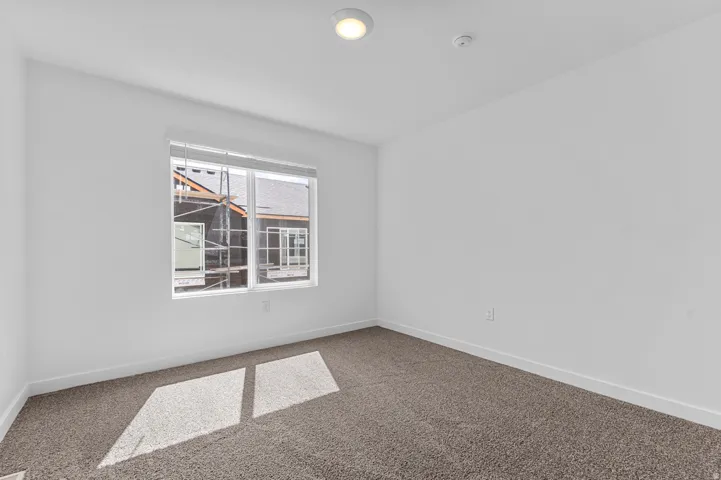Spacious room featuring clean white walls, neutral carpeting, a large window with blinds, and recessed lighting