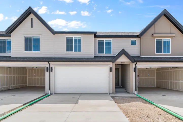 Modern multi-unit residence featuring a gabled roofline, light-toned siding, attached garages, and a paved driveway