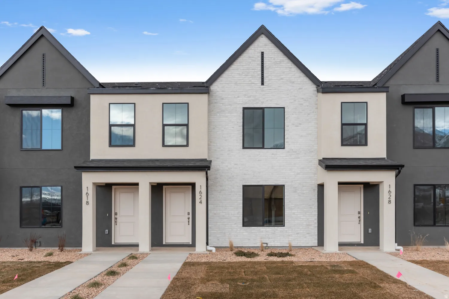 Contemporary townhome exterior featuring a white brick and grey stucco facade with black-framed windows
