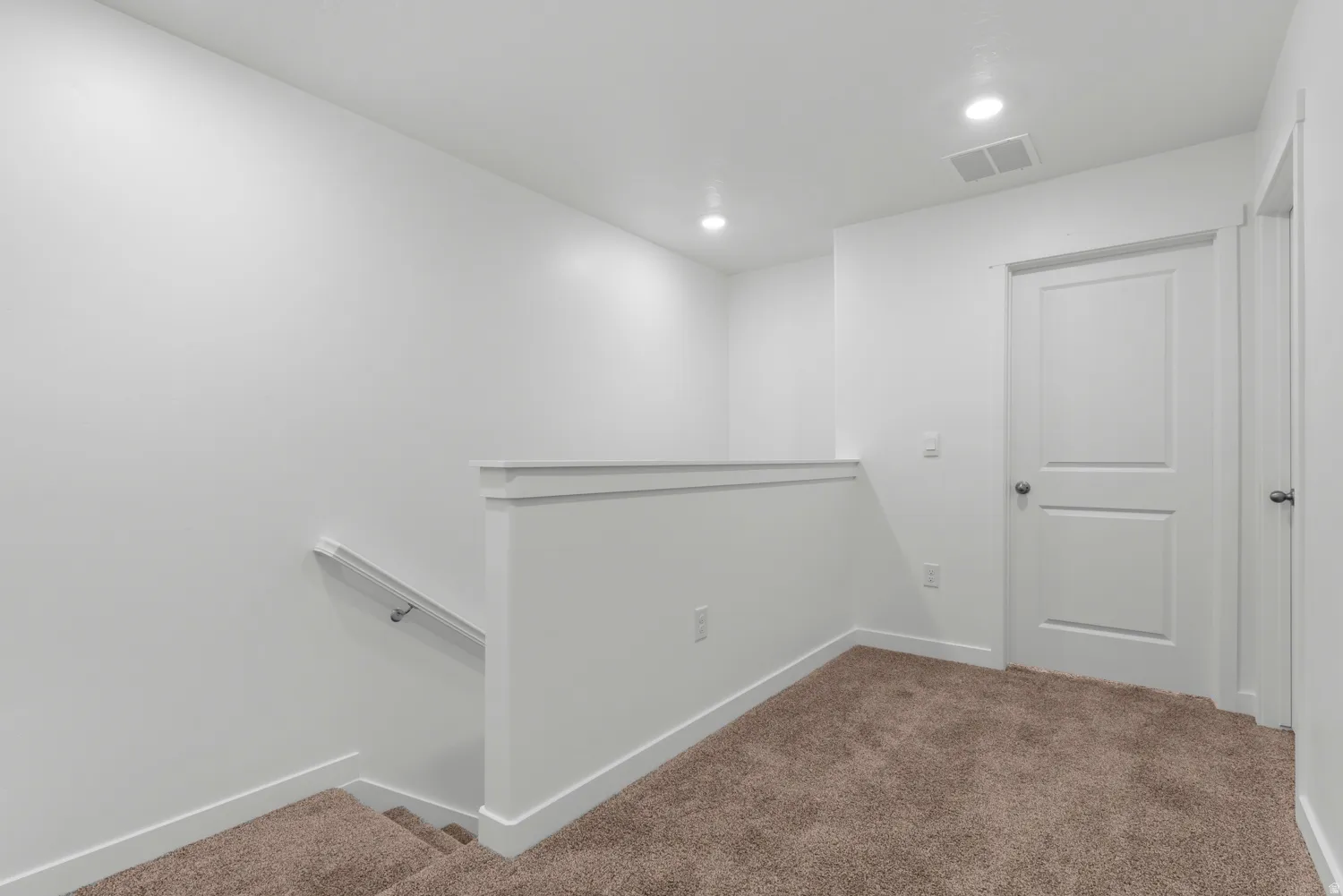 Carpeted upper landing featuring white walls, recessed lighting, and a two-panel interior door