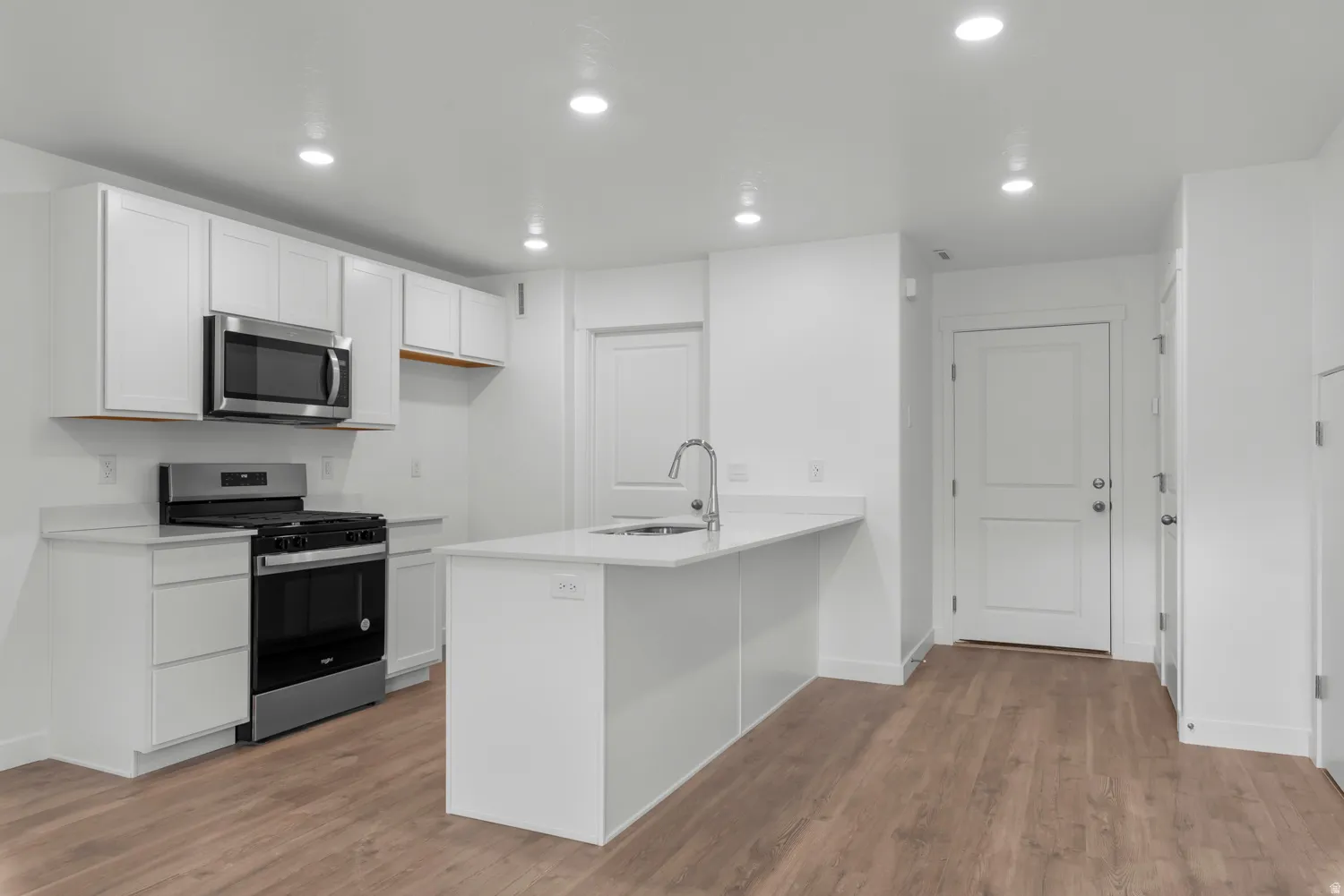 Modern kitchen featuring white cabinetry, stainless steel appliances, a center island with a sink, light-colored countertops, and wood-finish flooring