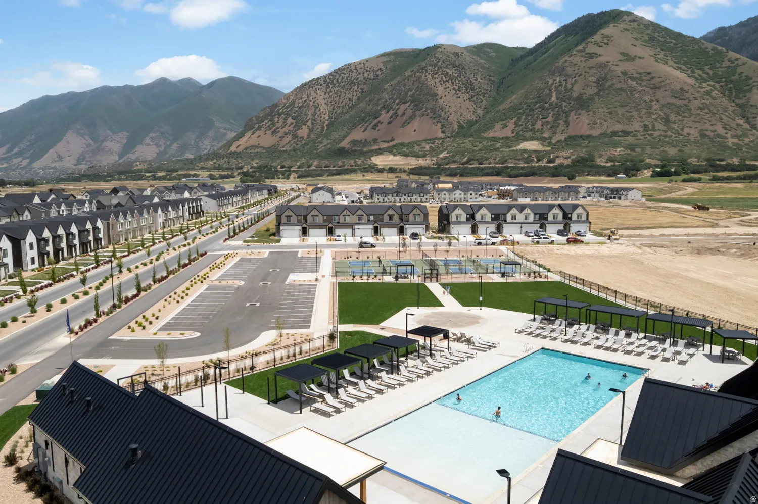Community swimming pool with an expansive concrete deck, shaded lounge areas, and surrounding green spaces
