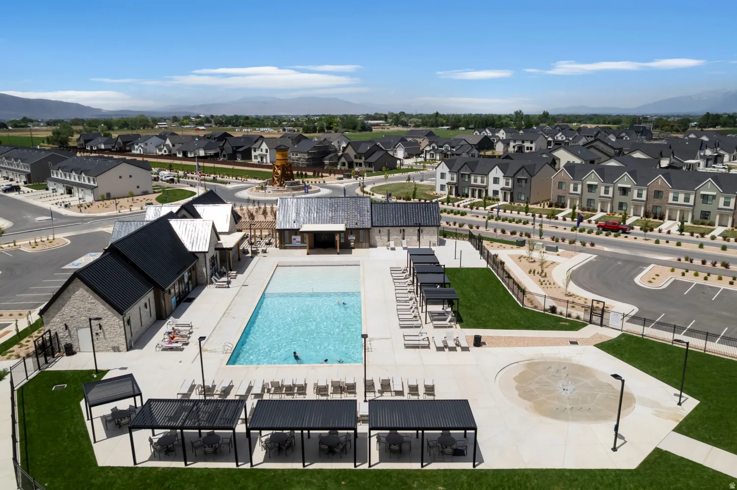 Outdoor community pool with surrounding paved deck, multiple lounge chairs, and shaded seating areas