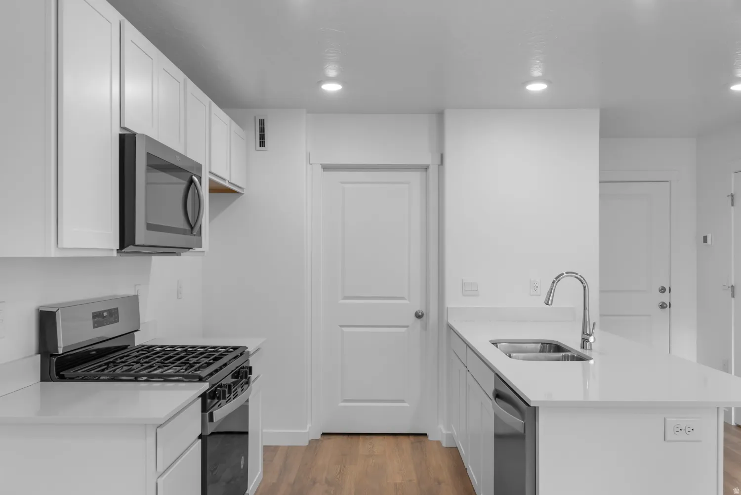 Contemporary kitchen featuring white cabinetry, light countertops, stainless steel appliances, and wood-finish flooring