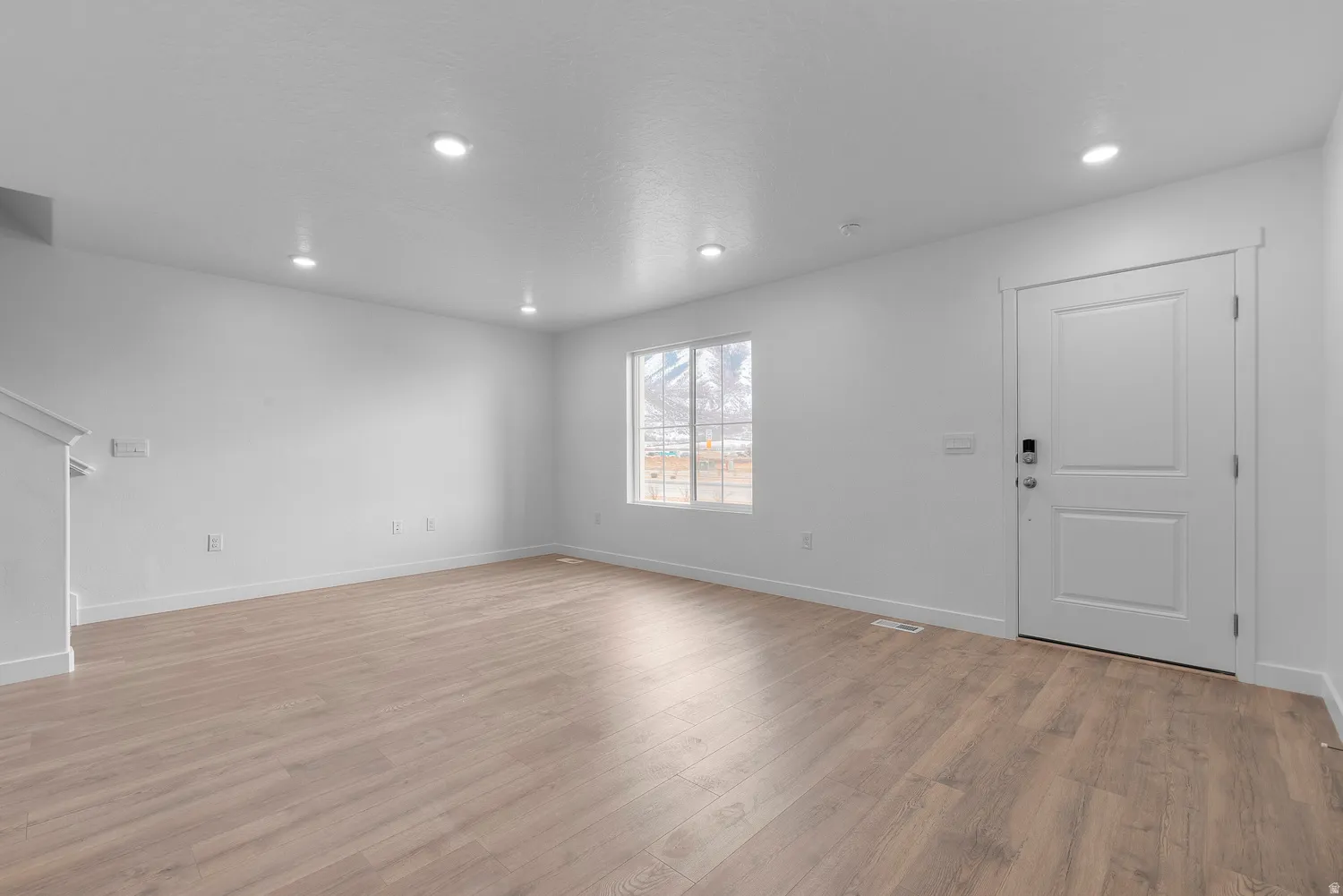 Spacious room featuring light wood-finish flooring, recessed lighting, and a neutral color palette