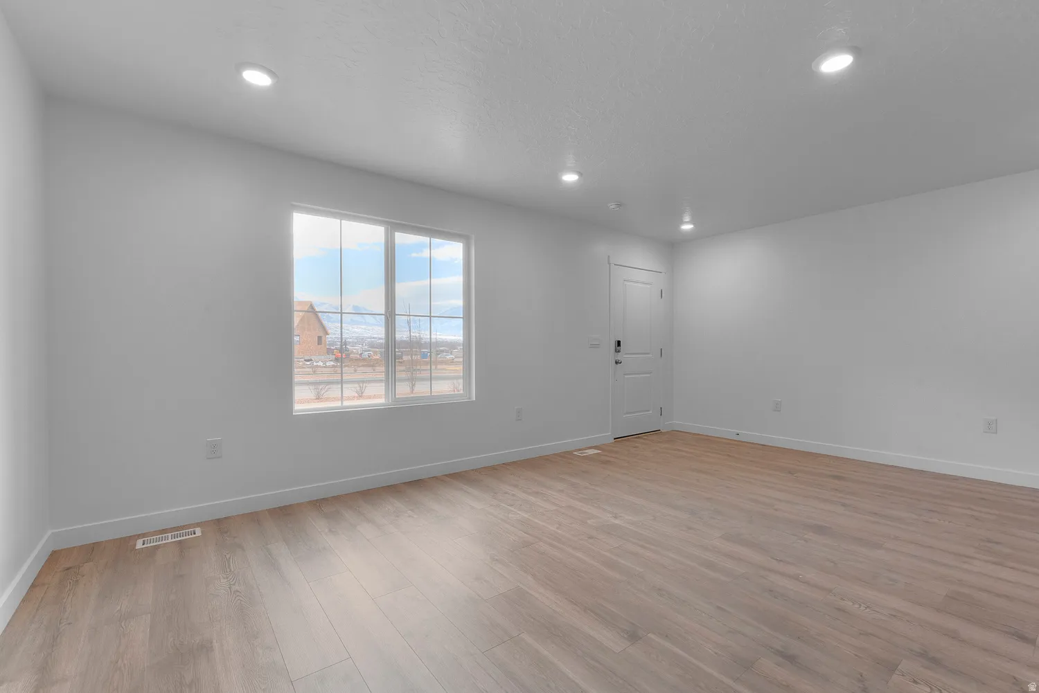 Bright room featuring expansive wood-finish flooring, recessed lighting, and a white paneled door