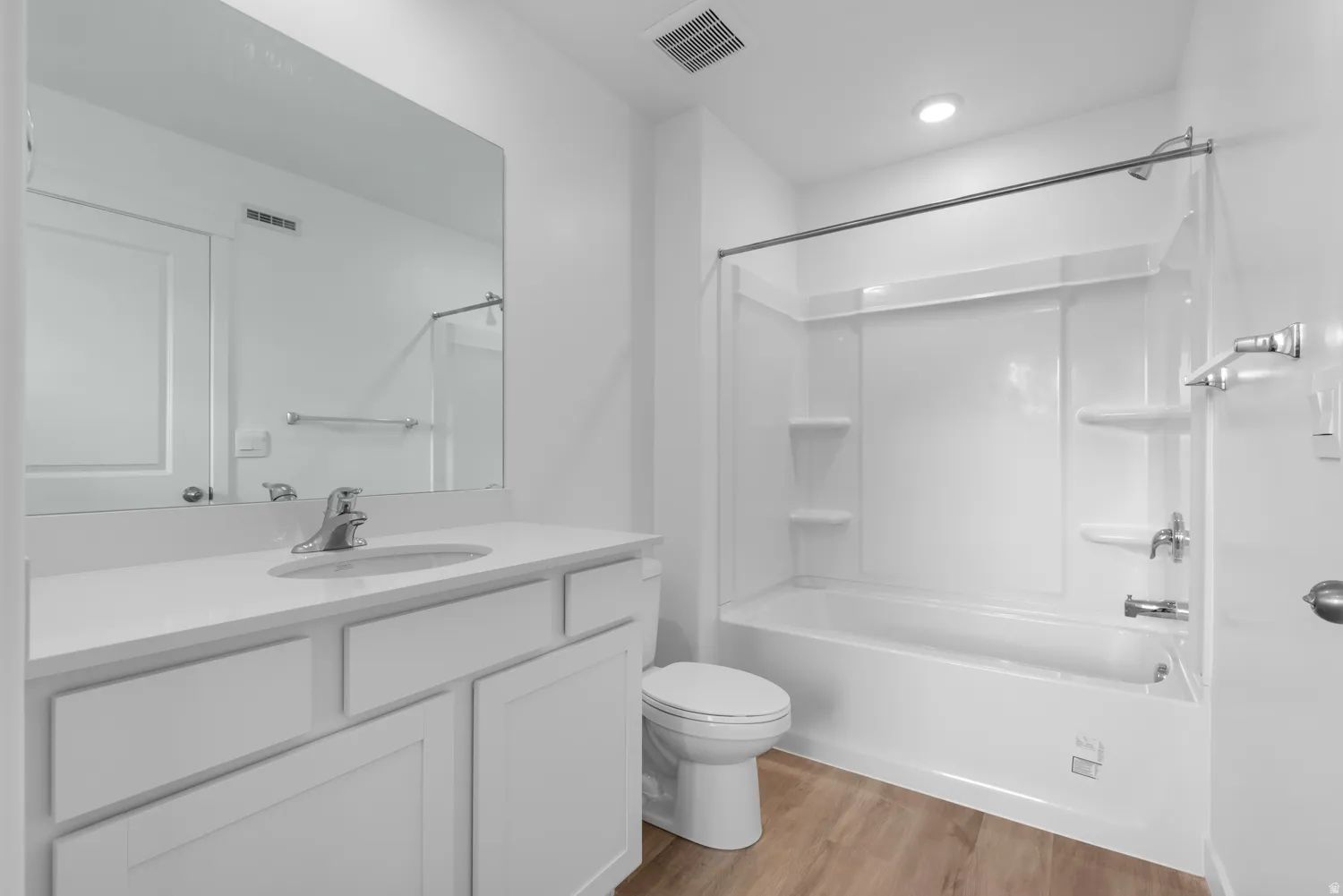 Bathroom featuring a white vanity with an integrated sink, polished chrome faucet, a large wall-mounted mirror, and wood-finish flooring