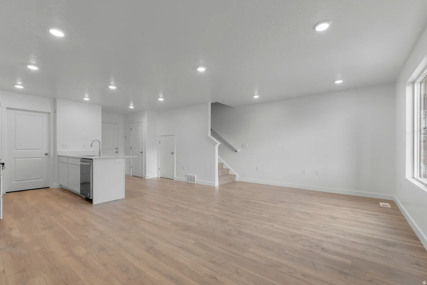 Open-concept living space featuring light wood-finish flooring, recessed lighting, and white walls