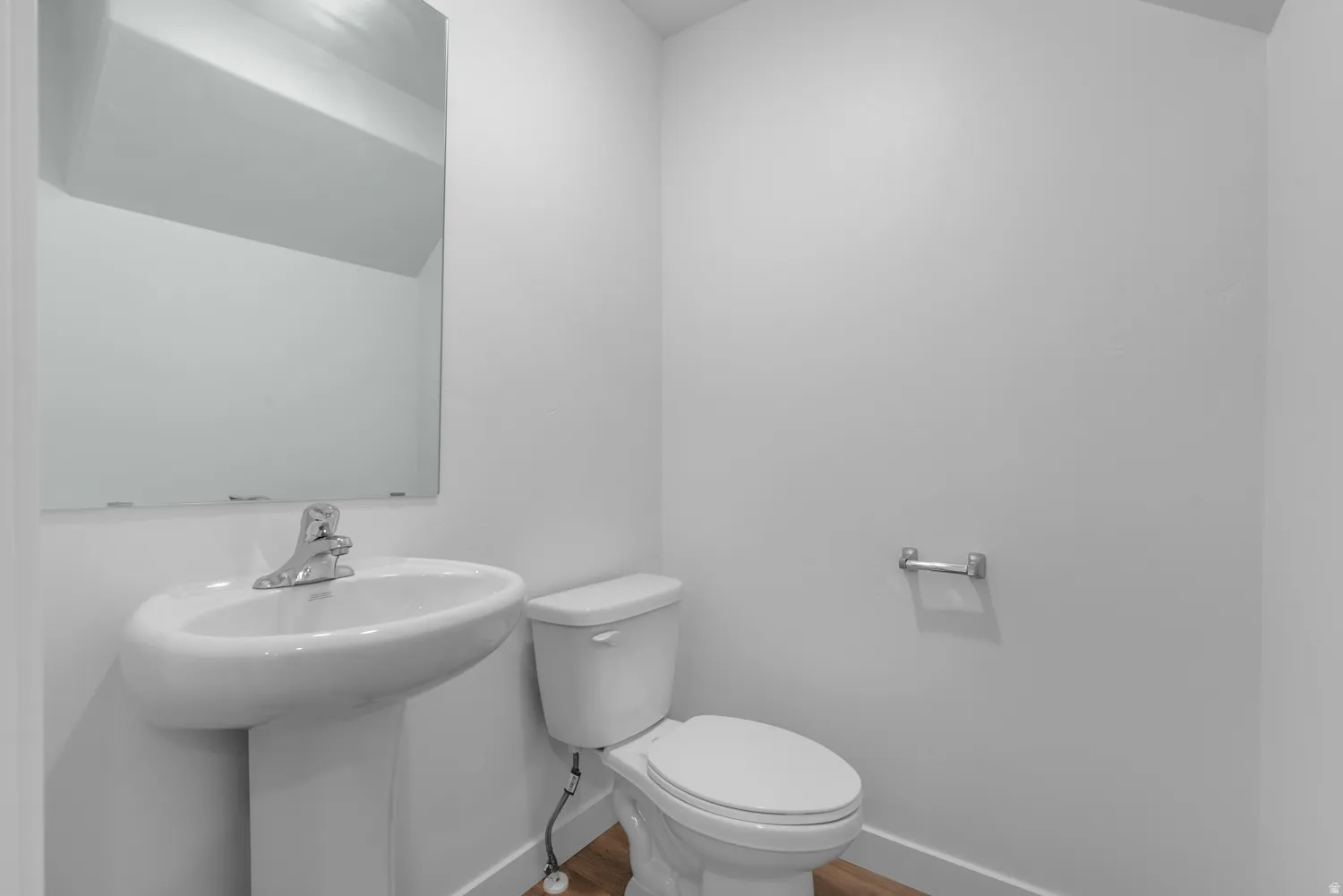 Pedestal sink with chrome faucet, wall-mounted mirror, white toilet, and wood-finish flooring