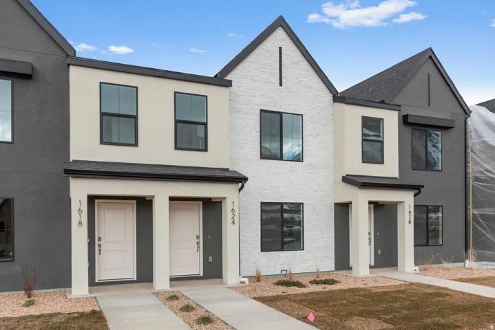 Modern townhome exterior featuring a white brick accent facade, dark gray and cream stucco finishes, black-framed windows, and a dark asphalt shingle roof