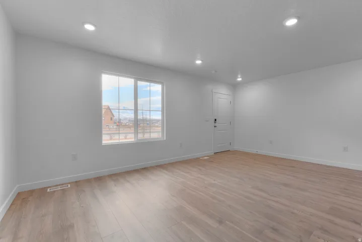 Bright room featuring expansive wood-finish flooring, recessed lighting, and a white paneled door