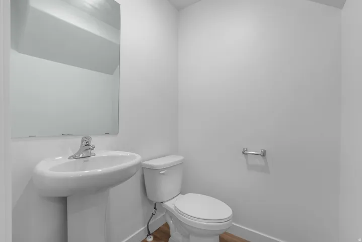 Pedestal sink with chrome faucet, wall-mounted mirror, white toilet, and wood-finish flooring