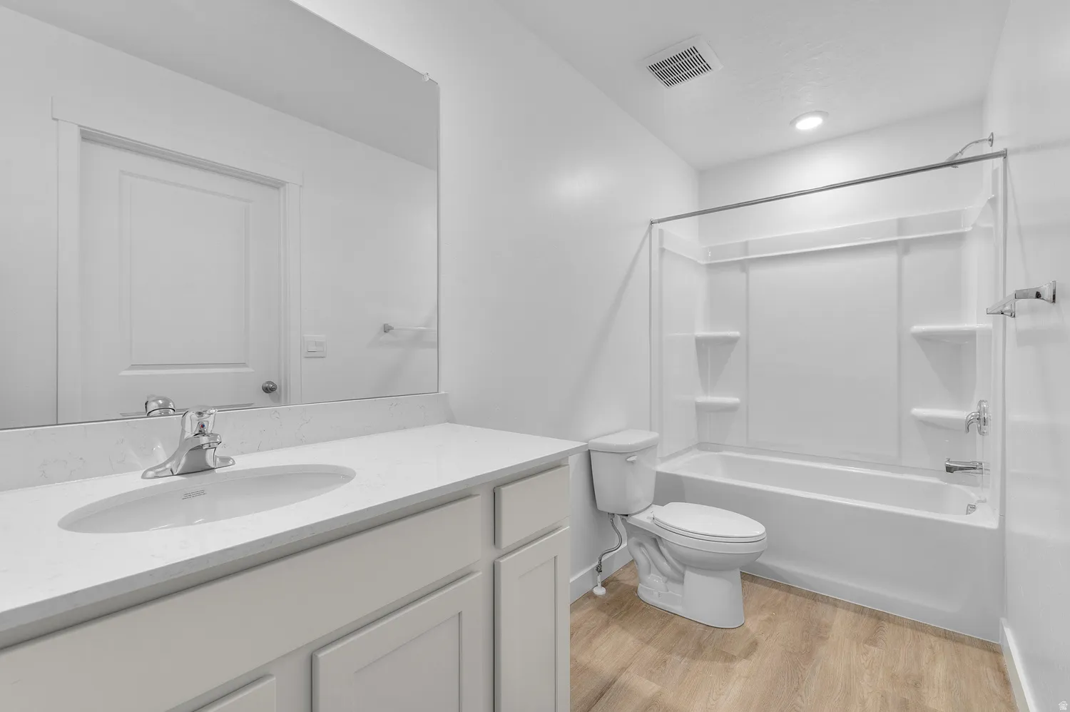 Bathroom featuring a spacious vanity with an undermount sink, a large wall-mounted mirror, a tub and shower combination with an integrated shelving system, recessed lighting, and wood-finish flooring