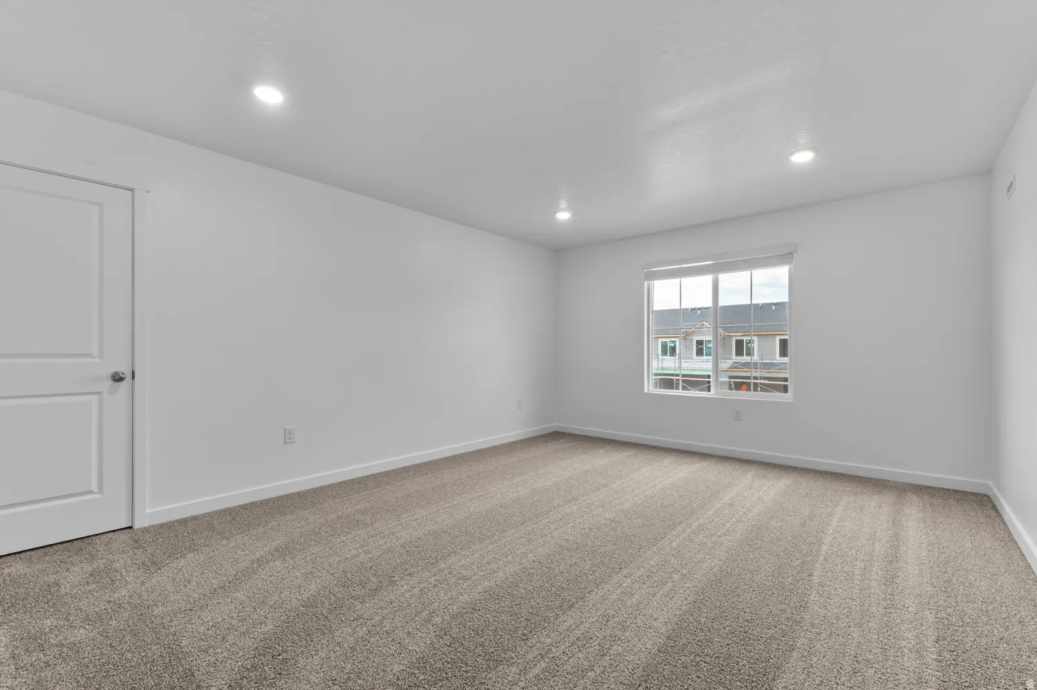 Room featuring light gray carpeting, recessed ceiling lighting, a white two-panel door with a brushed nickel knob, and a window with a white frame and blind