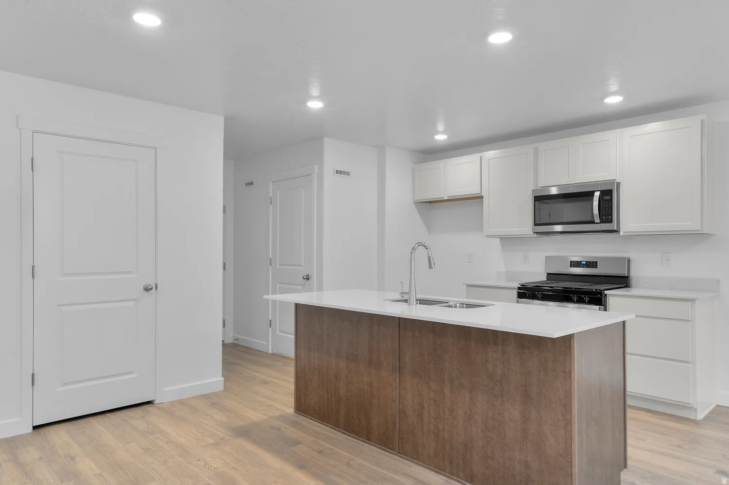 Kitchen featuring a spacious island with an integrated sink, white cabinetry, stainless steel appliances, wood-finish flooring, and recessed lighting