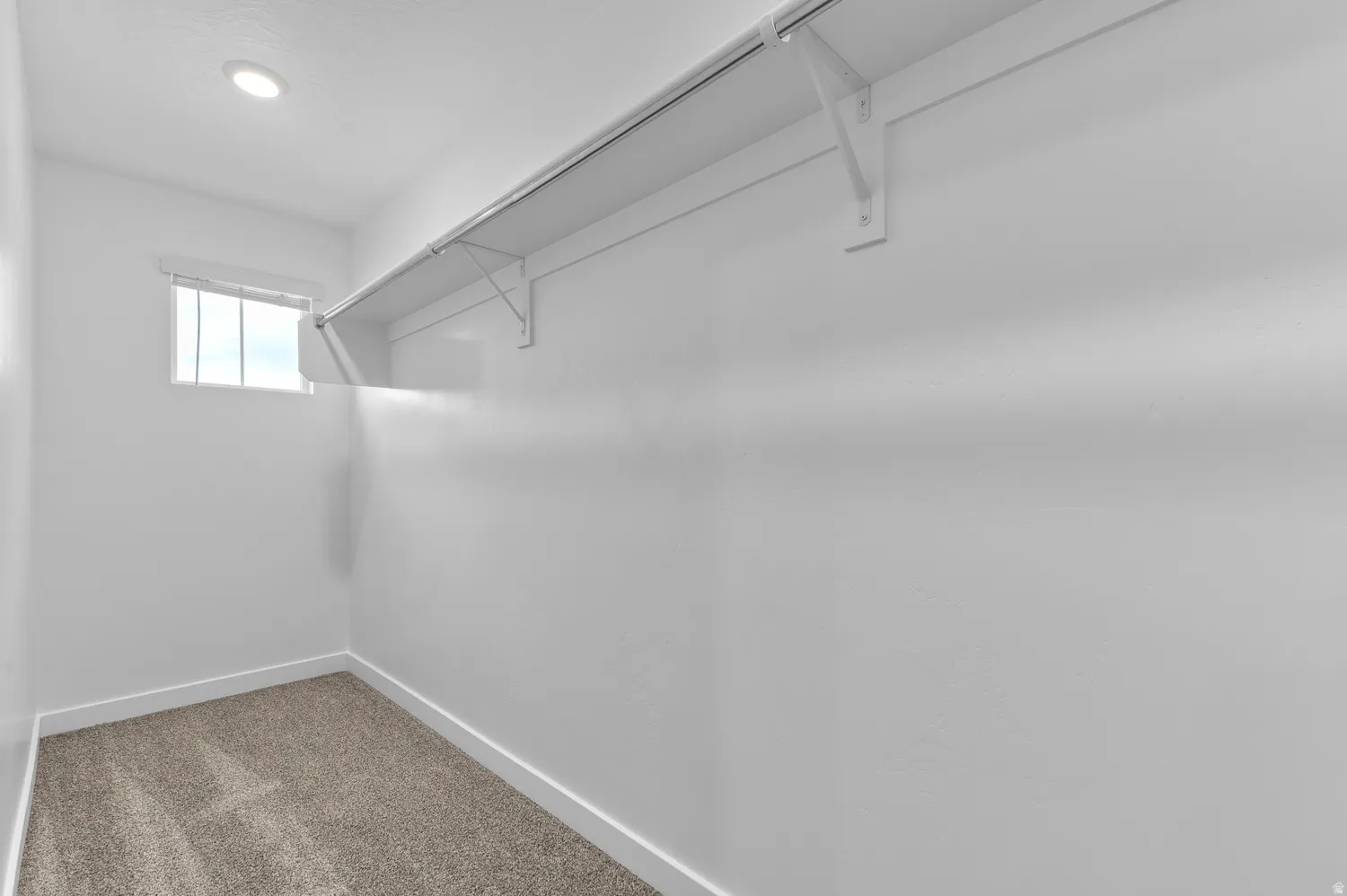 Walk-in closet featuring built-in shelving, hanging rod, recessed lighting, and a window for natural illumination