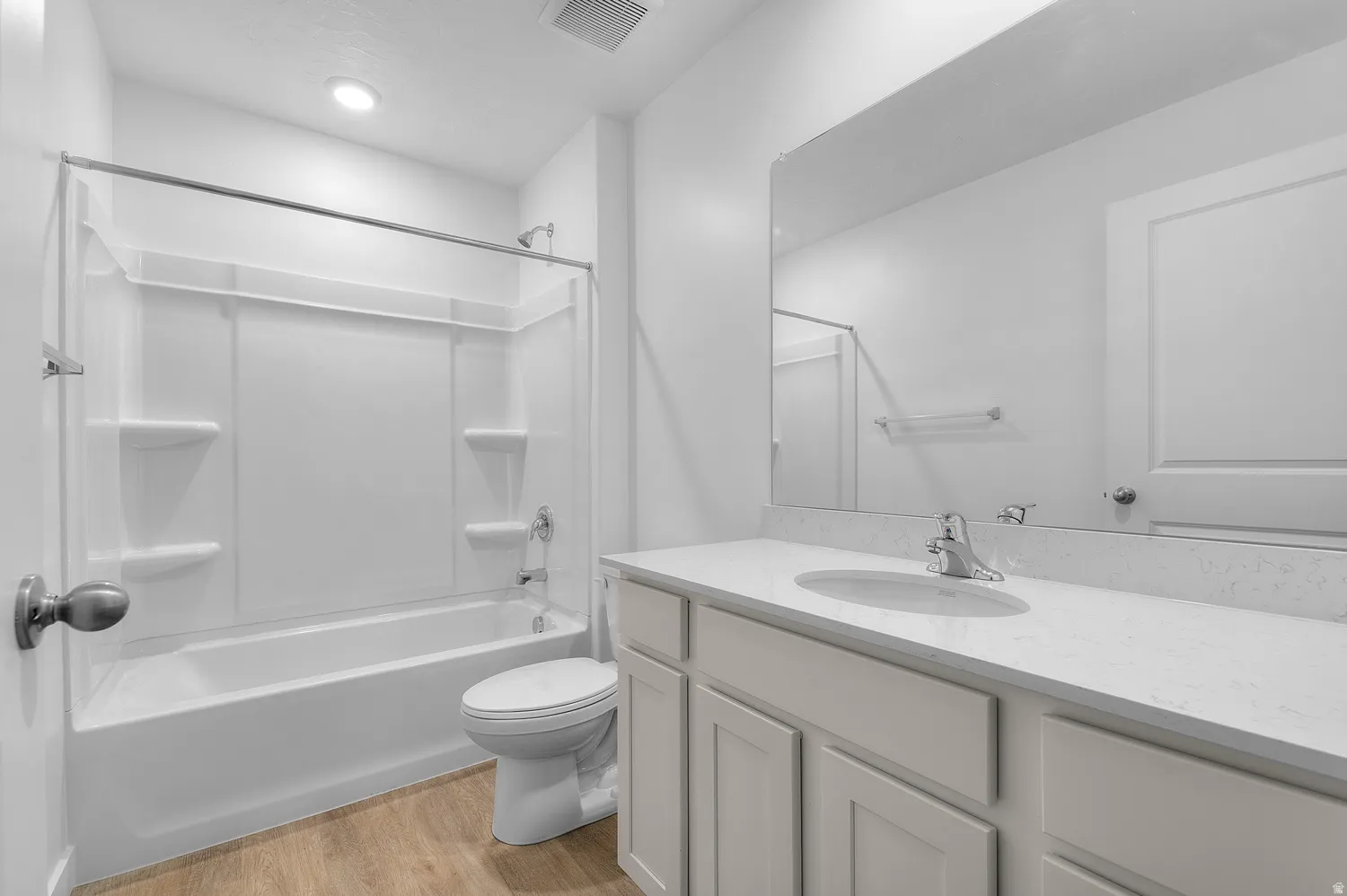 Bathroom featuring a white vanity with an integrated sink and light-colored countertop, large wall-mounted mirror, white tub with shower surround, and wood-finish flooring