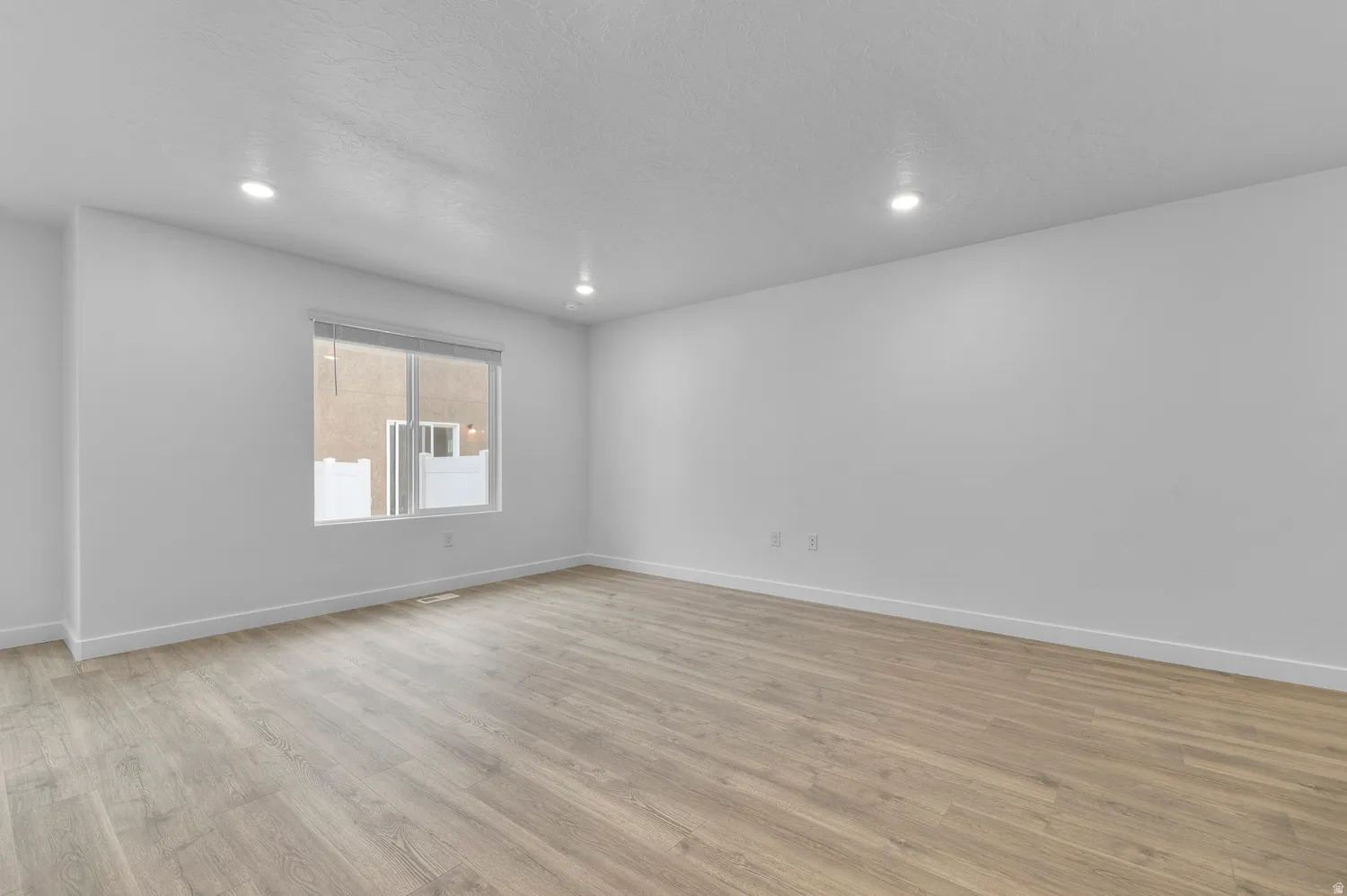Spacious room featuring light wood-finish flooring, recessed lighting, and a window with blinds