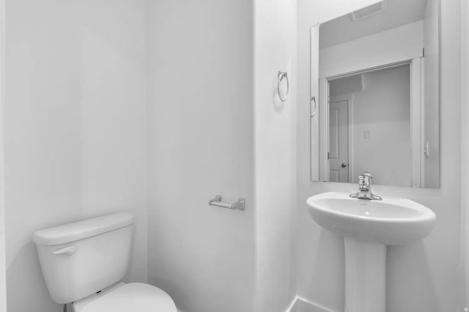 Pedestal sink with mirror, toilet, and chrome fixtures