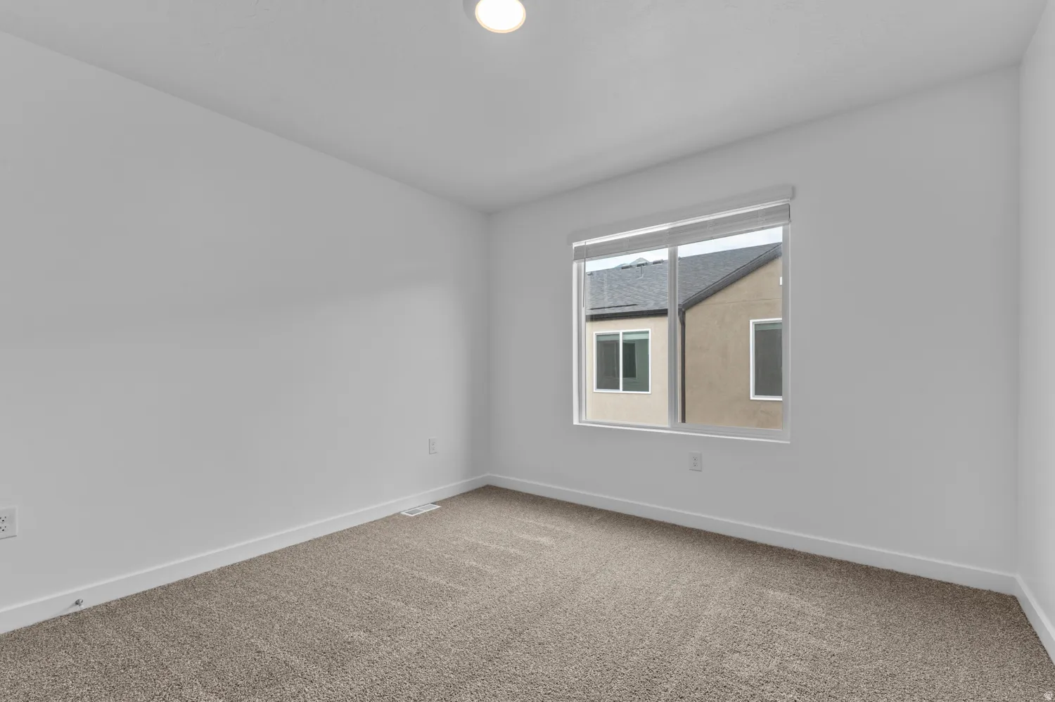 Bright interior space featuring a window with integrated blinds, textured carpet flooring, white painted walls, and a ceiling-mounted light fixture
