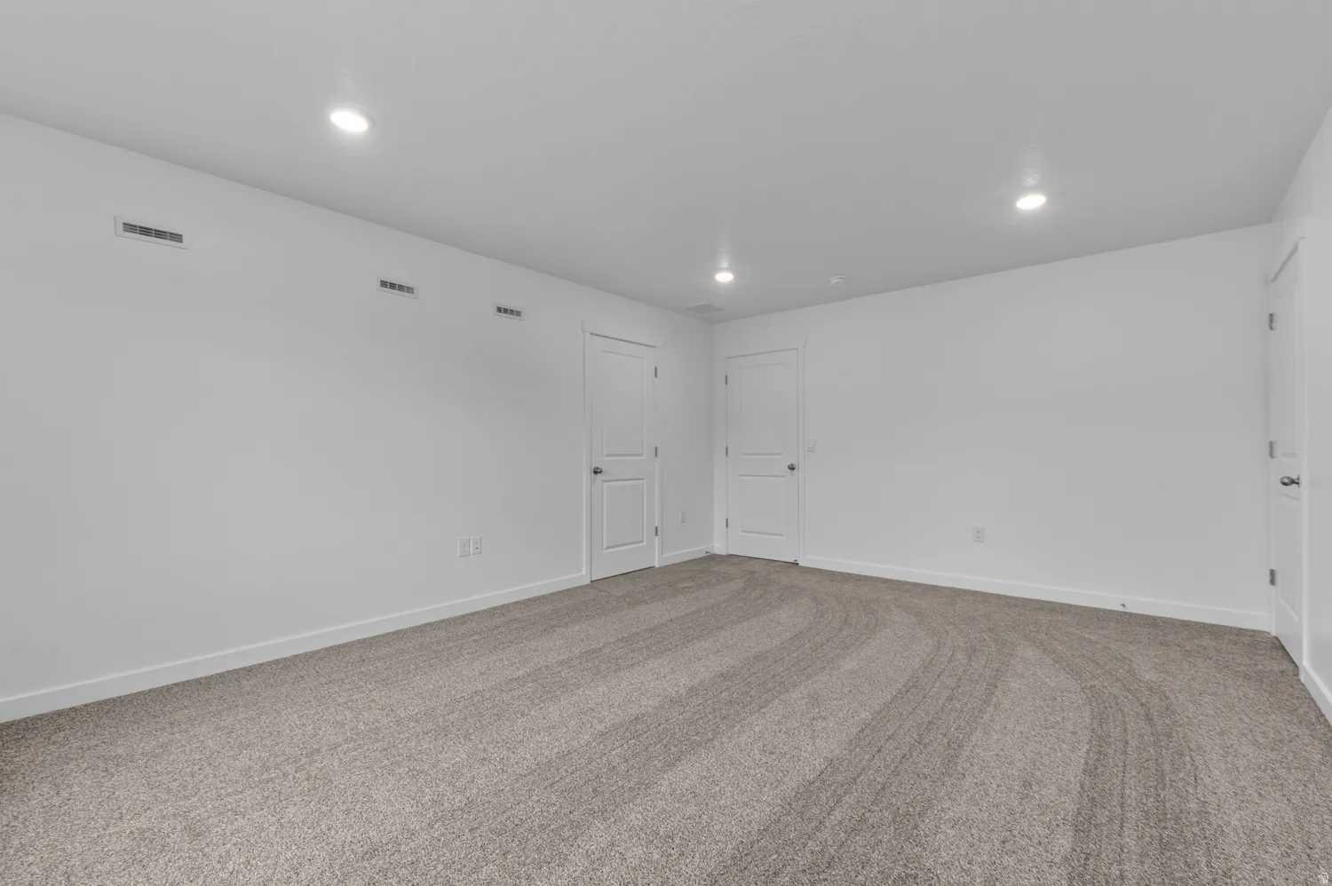 Spacious room featuring light-colored carpeting, white walls, and recessed lighting fixtures