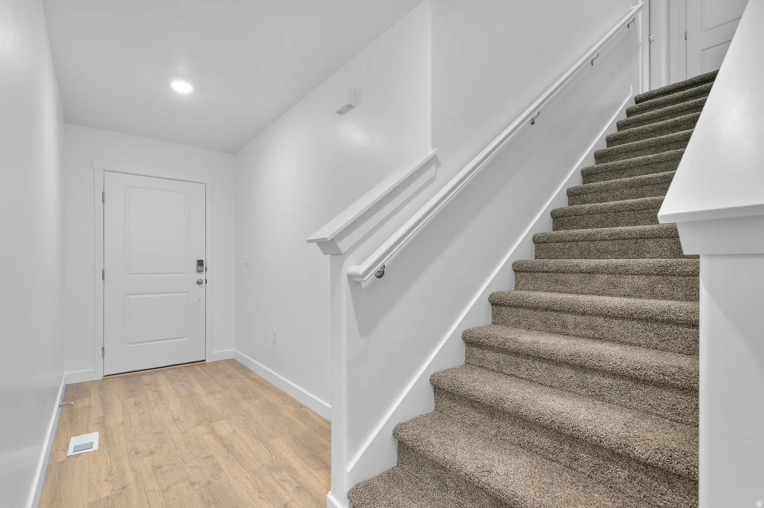 Entryway featuring wood-finish flooring, a white paneled door with contemporary hardware, a recessed ceiling light, and a carpeted staircase with white railings