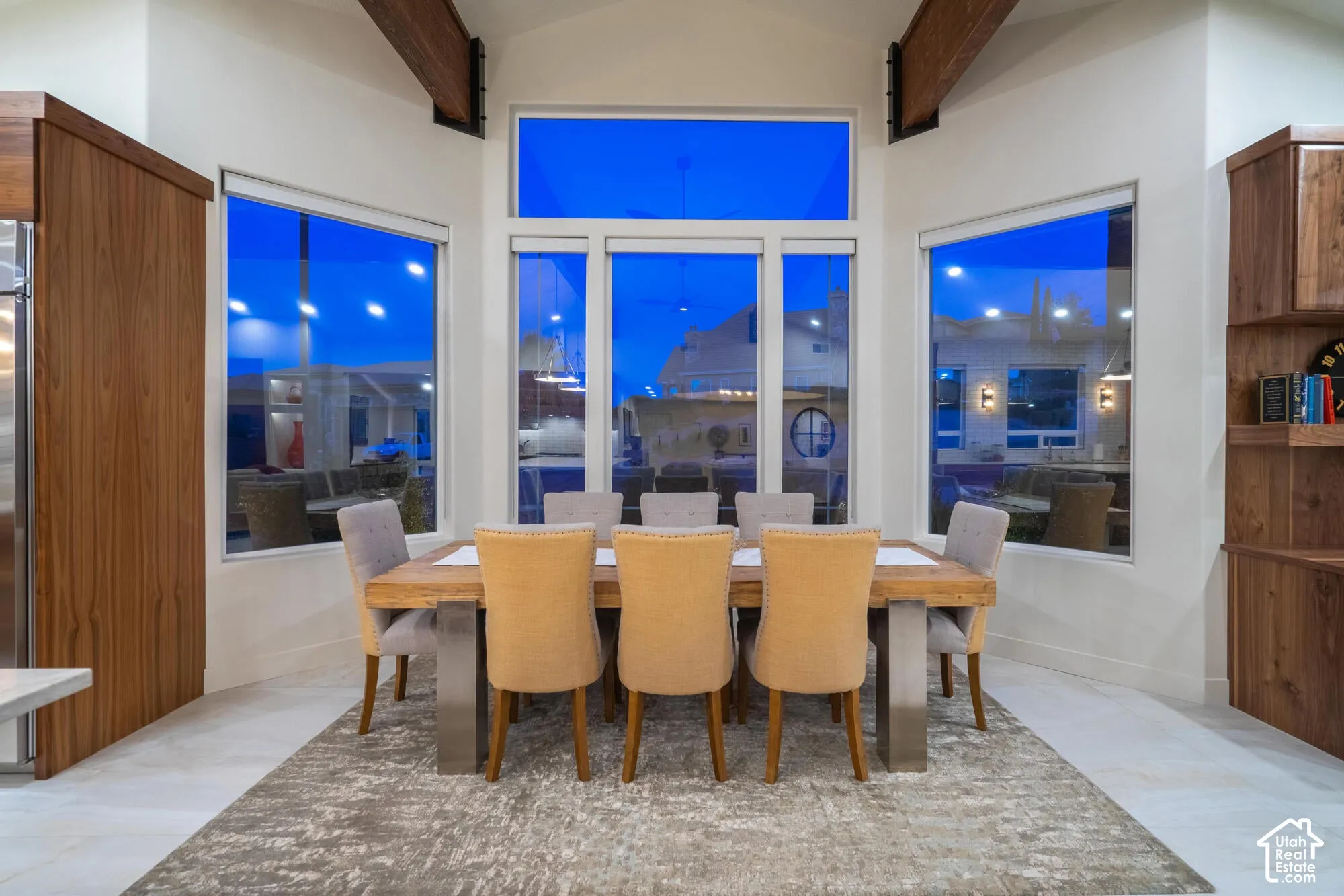 Dining area featuring high ceilings with exposed wood beams, a prominent window wall, light-toned floor tile, and built-in wood cabinetry