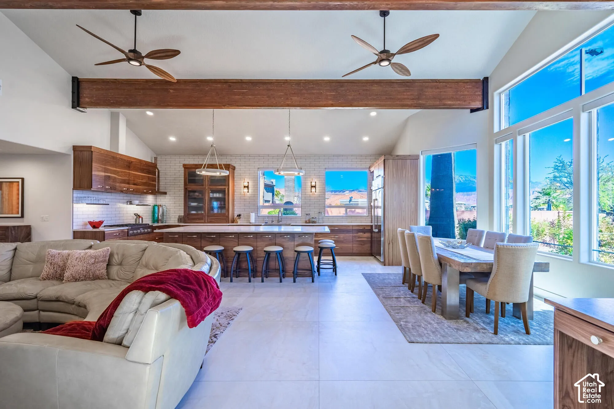 Spacious open-concept living area featuring a kitchen with custom wood cabinetry and white subway tile backsplash, an island with seating, and a dining area with a large window wall