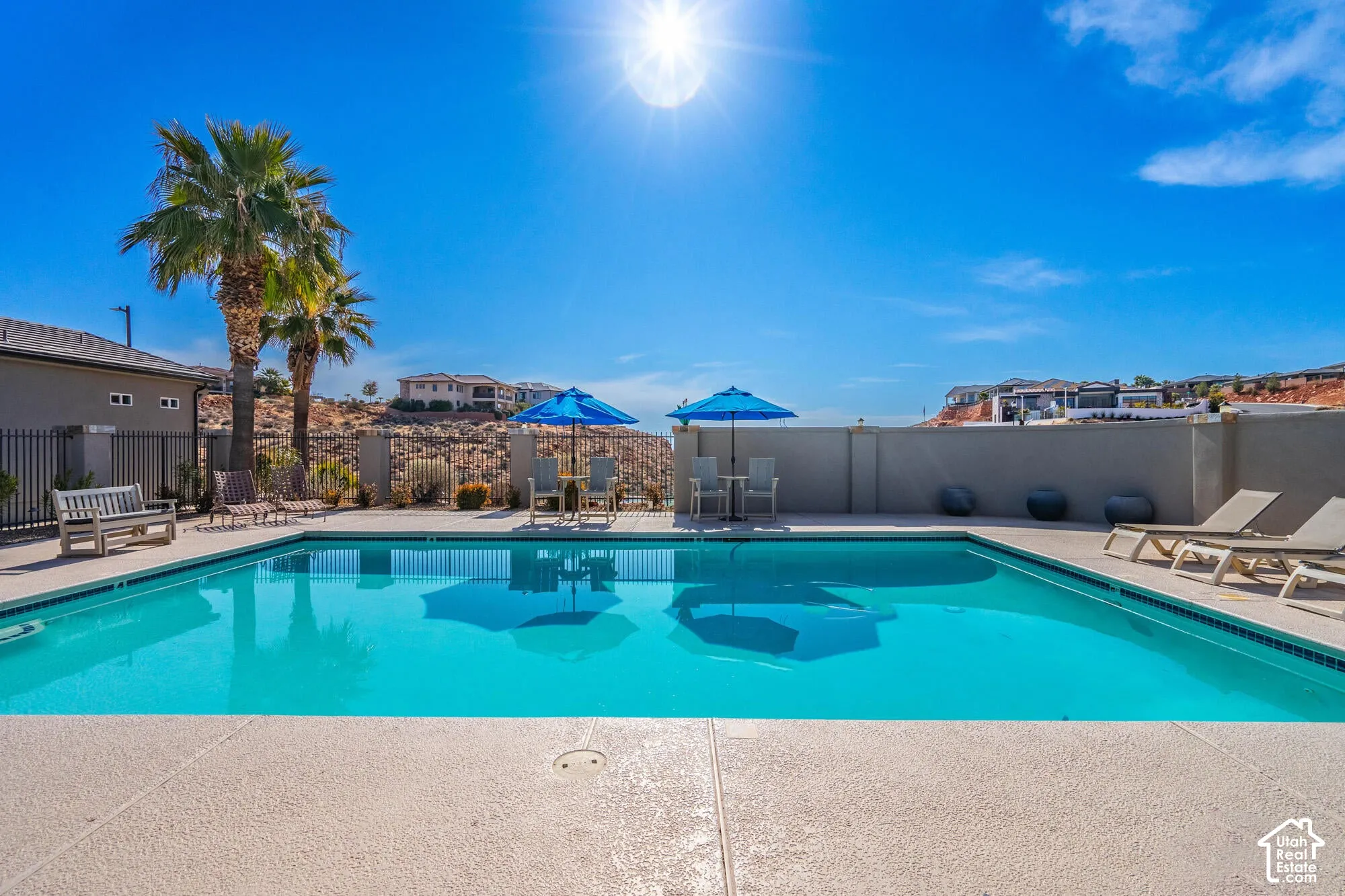 Outdoor swimming pool with a concrete surround, enclosed by a perimeter wall and black metal fencing