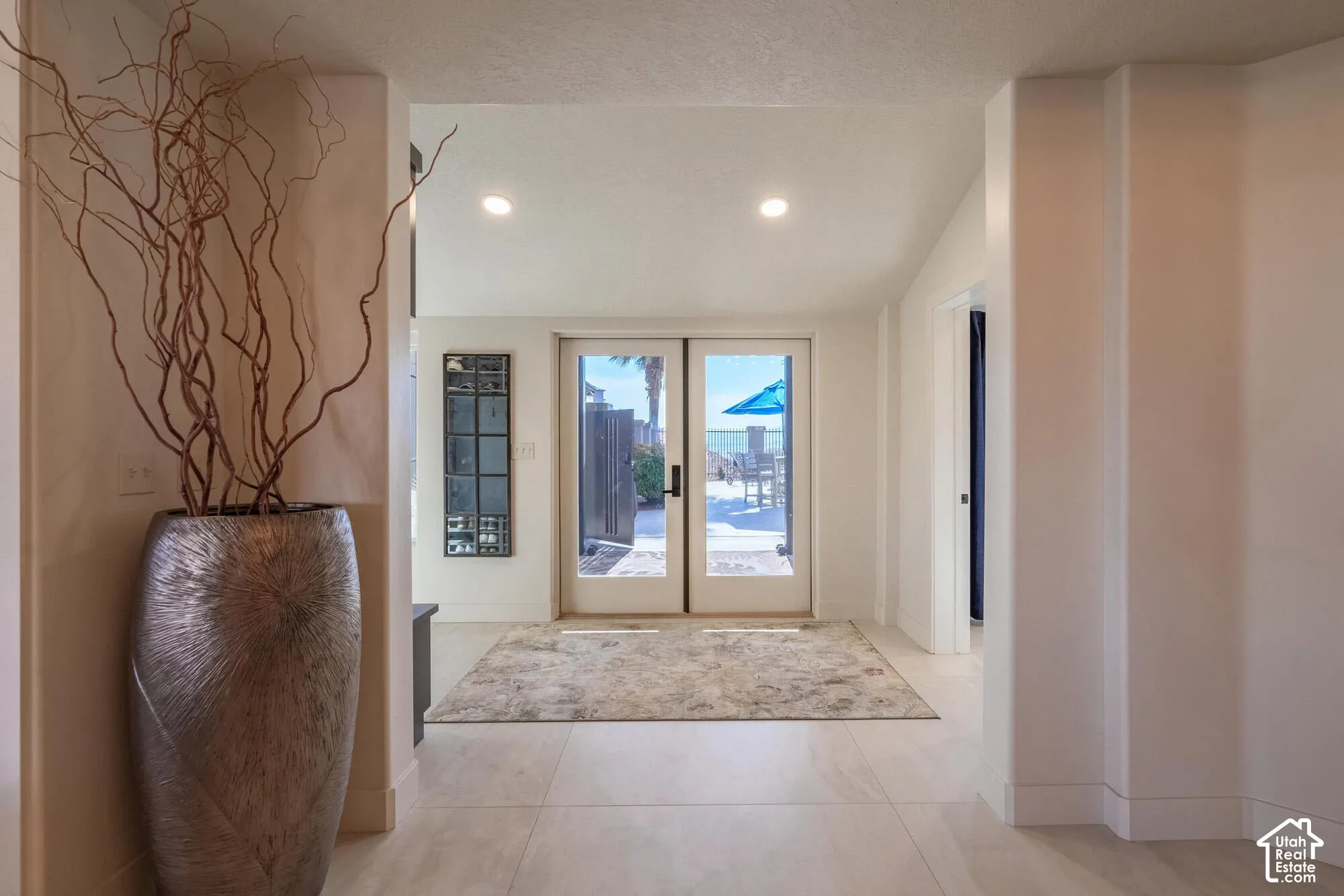 Glass-paned double doors leading to an outdoor patio with a visible ocean backdrop, recessed lighting, and light-toned flooring