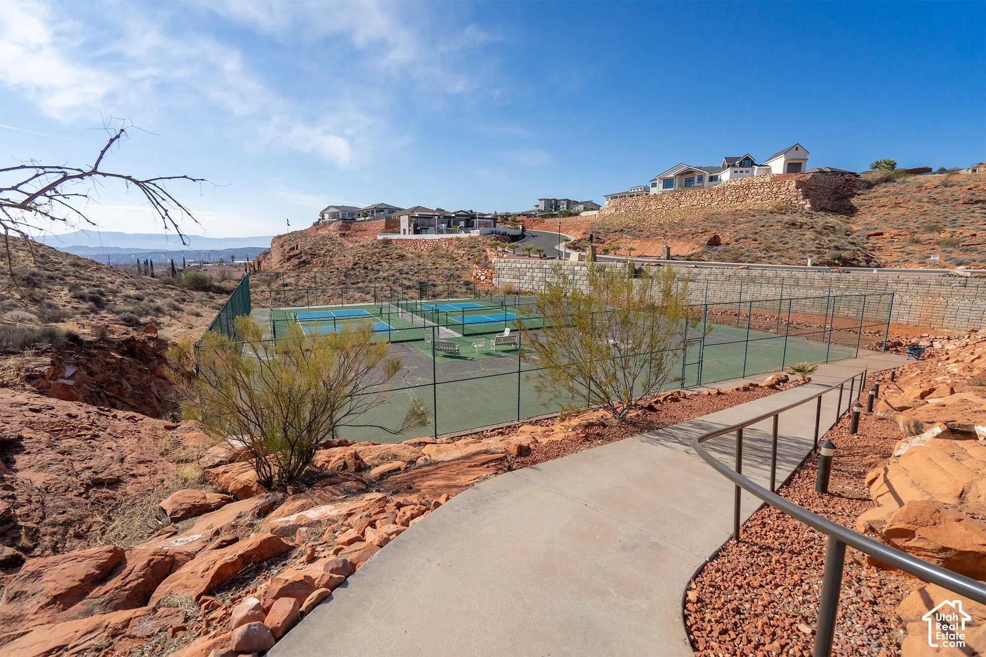 Multiple outdoor tennis courts featuring blue and green playing surfaces, surrounded by fencing