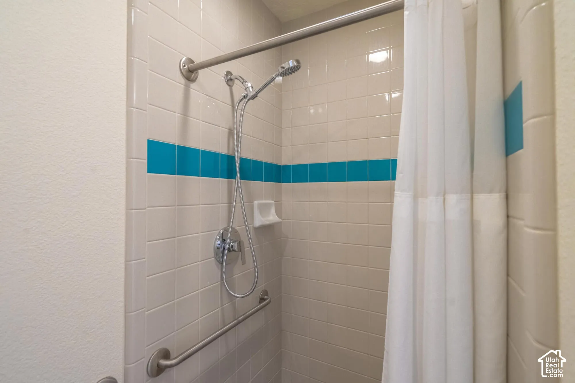 Tiled shower with a vibrant blue accent stripe, chrome fixtures, and a curved shower rod