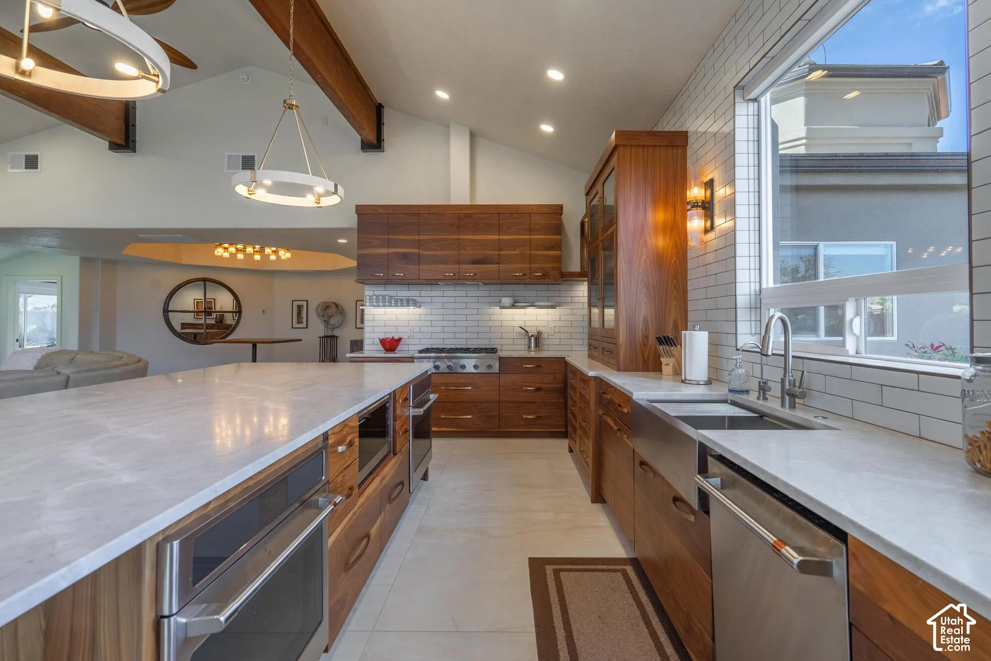 Spacious kitchen featuring a large central island with integrated oven, extensive wood cabinetry, white subway tile backsplash, and a deep basin sink beneath a wide window