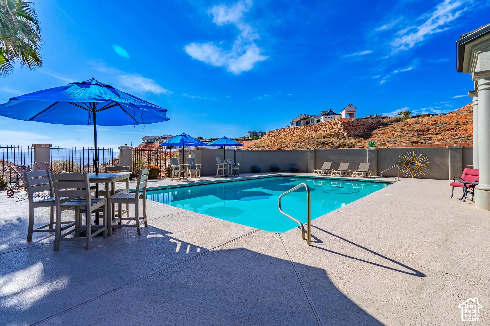 Expansive outdoor pool area featuring a perimeter fence, a concrete patio surround, a pool entry handrail, and a decorative sunburst wall accent