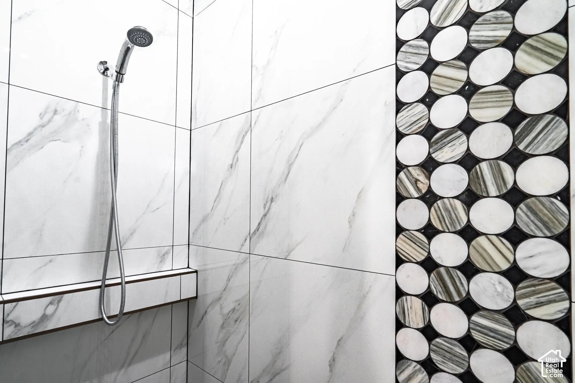 Shower enclosure featuring large format white marble-look tiles with dark grout