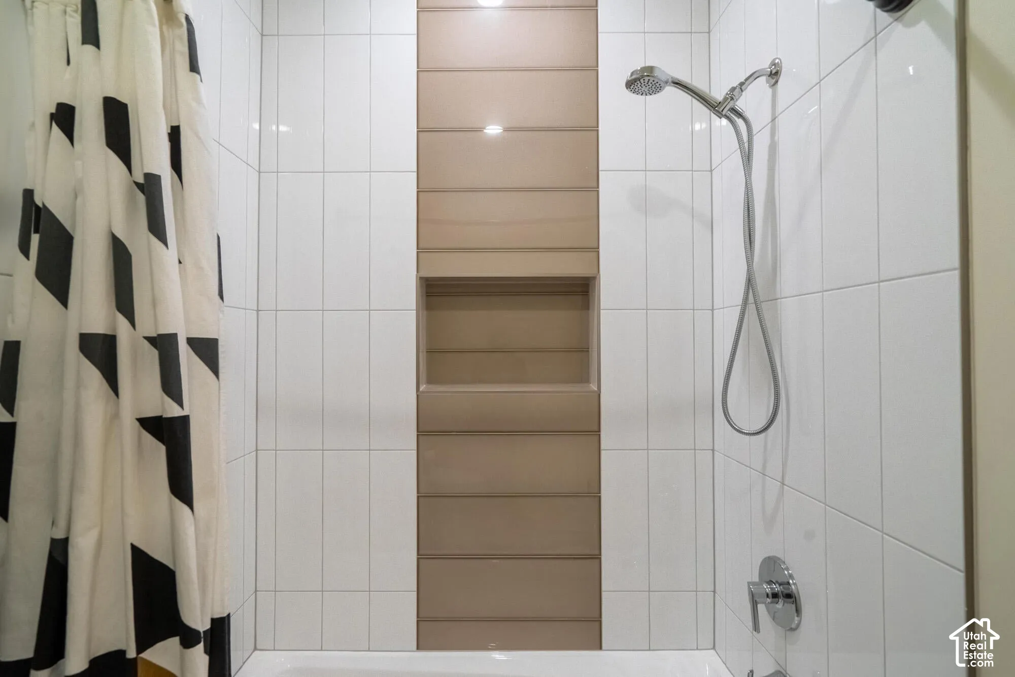 Bathtub and shower combination featuring white subway tile, a recessed niche, and a contrasting horizontal tile accent band
