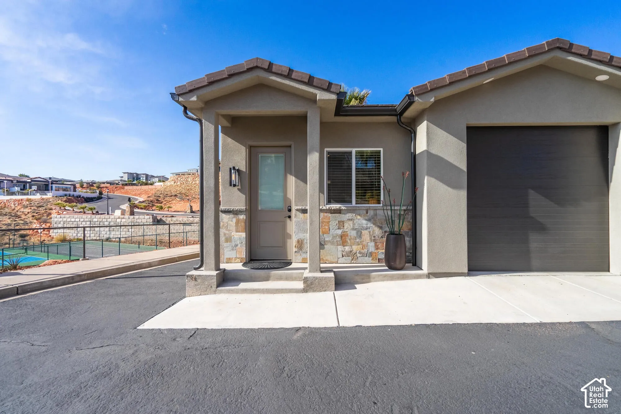 Stucco exterior featuring stacked stone accents, a covered entry with an outdoor sconce, a dark wood-finish front door with an opaque glass insert, a dark garage door, and a concrete driveway