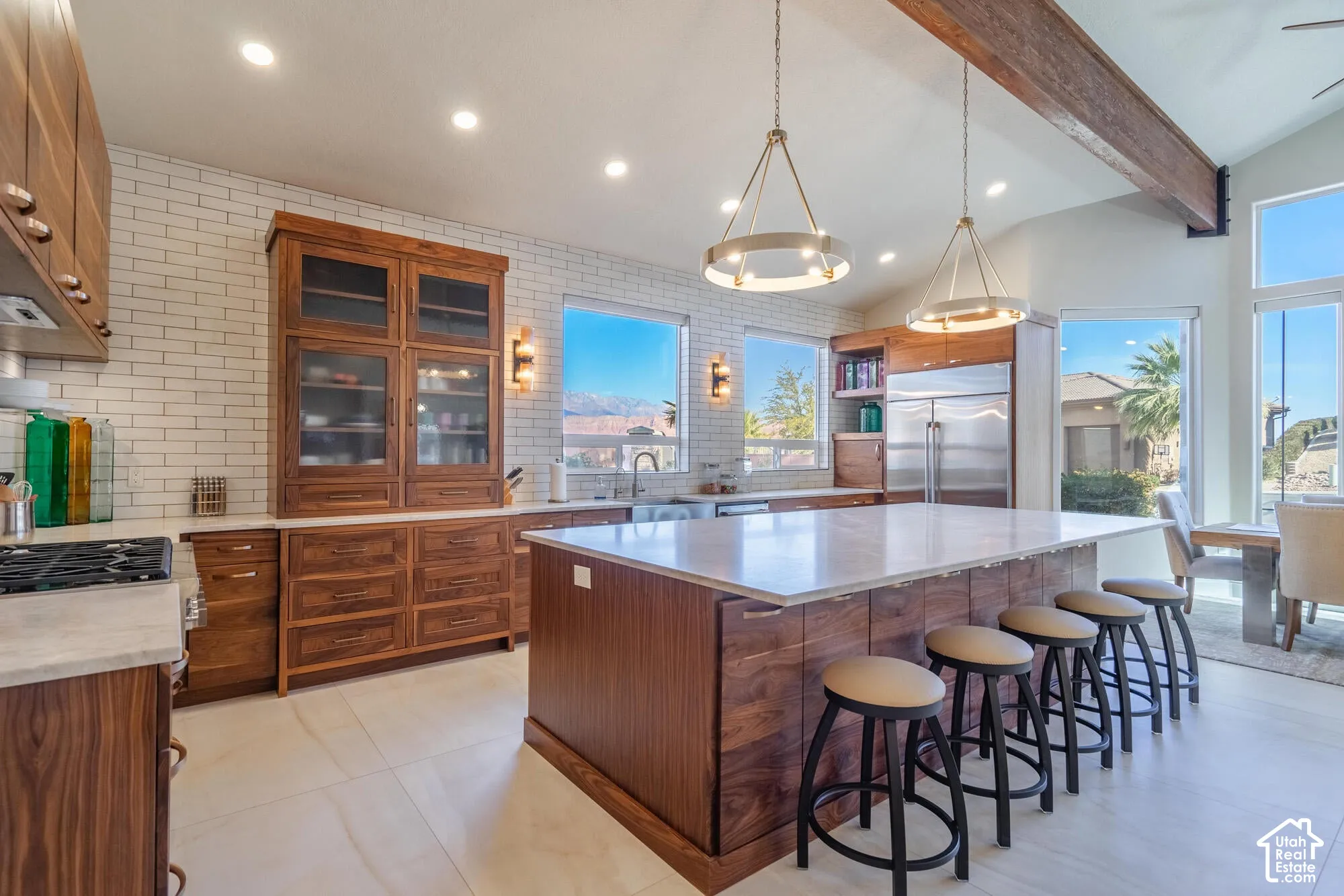 Gourmet kitchen featuring a large central island with seating, dark wood-finish cabinetry, tile backsplash, stainless steel appliances, and abundant natural light from multiple windows