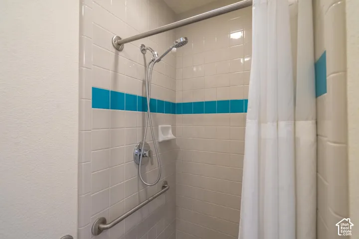 Tiled shower with a vibrant blue accent stripe, chrome fixtures, and a curved shower rod