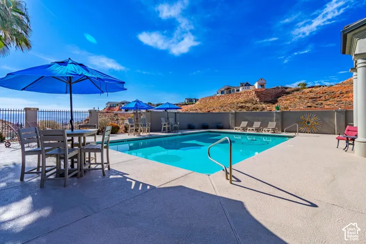Expansive outdoor pool area featuring a perimeter fence, a concrete patio surround, a pool entry handrail, and a decorative sunburst wall accent