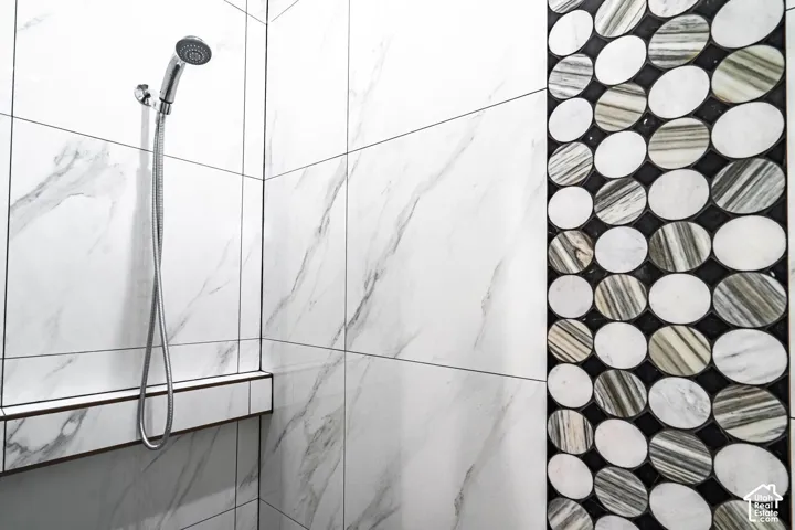 Shower enclosure featuring large format white marble-look tiles with dark grout