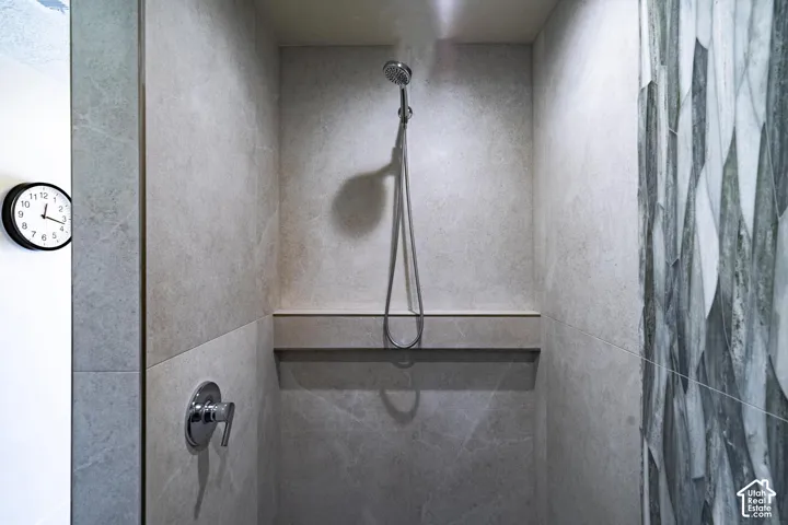 Walk-in shower with light gray stone-finish wall tile, built-in shelf, and handheld showerhead