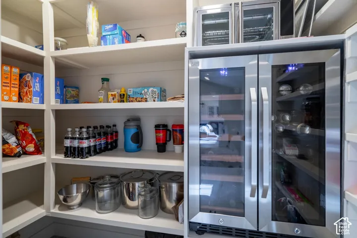 Walk-in pantry featuring extensive built-in shelving, a stainless steel dual-zone beverage refrigerator, and a compact stainless steel wine cooler